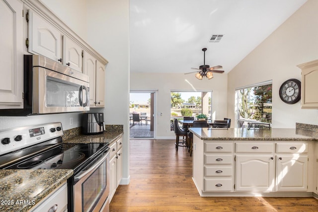 kitchen featuring light hardwood / wood-style floors, stainless steel appliances, dark stone counters, and kitchen peninsula