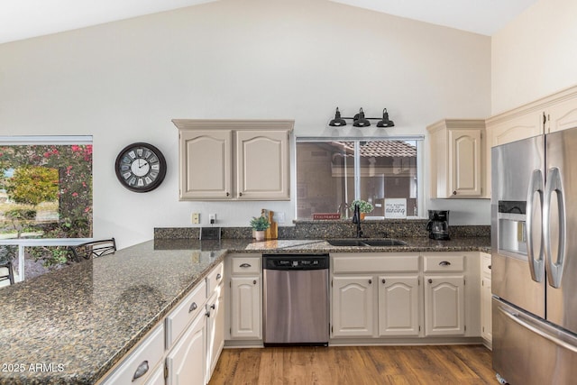 kitchen featuring stainless steel appliances, light hardwood / wood-style floors, sink, and dark stone counters