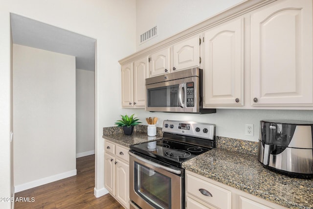 kitchen featuring appliances with stainless steel finishes, dark hardwood / wood-style floors, and dark stone counters