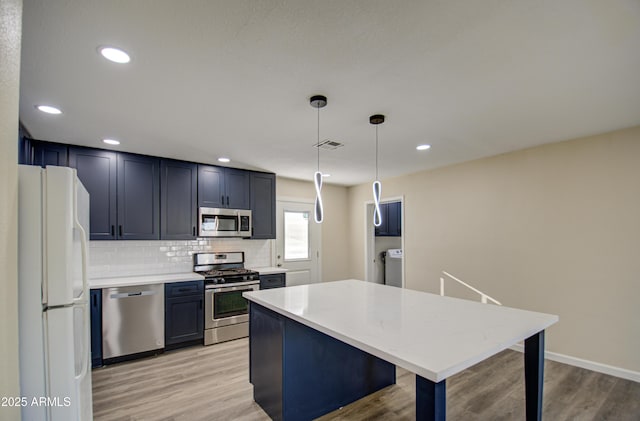 kitchen featuring backsplash, light wood-type flooring, hanging light fixtures, and appliances with stainless steel finishes