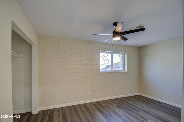 spare room featuring dark hardwood / wood-style flooring, ceiling fan, and brick wall