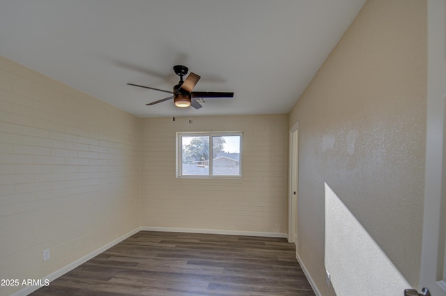 unfurnished room with dark hardwood / wood-style floors, ceiling fan, and brick wall