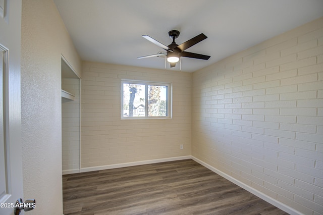 empty room with dark hardwood / wood-style flooring, ceiling fan, and brick wall