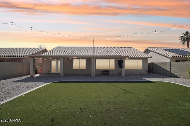 back of property at dusk with a patio area, a fenced backyard, stucco siding, and a tile roof