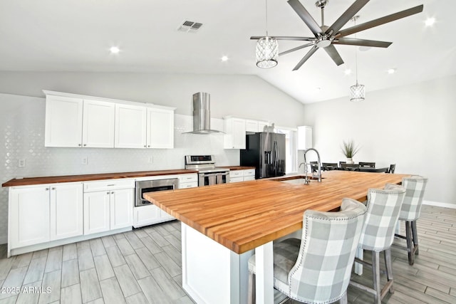 kitchen with wall chimney range hood, visible vents, appliances with stainless steel finishes, a sink, and butcher block countertops