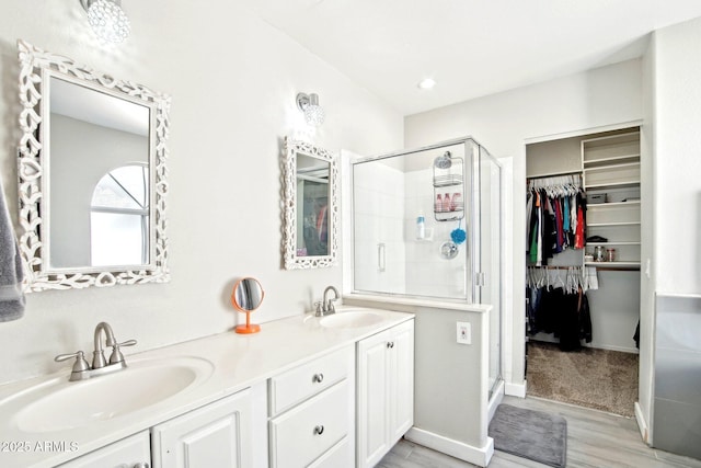 full bathroom featuring a sink, a walk in closet, a stall shower, and double vanity