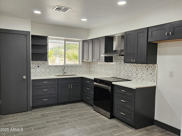 kitchen featuring tasteful backsplash, visible vents, range with electric stovetop, wall chimney exhaust hood, and a sink