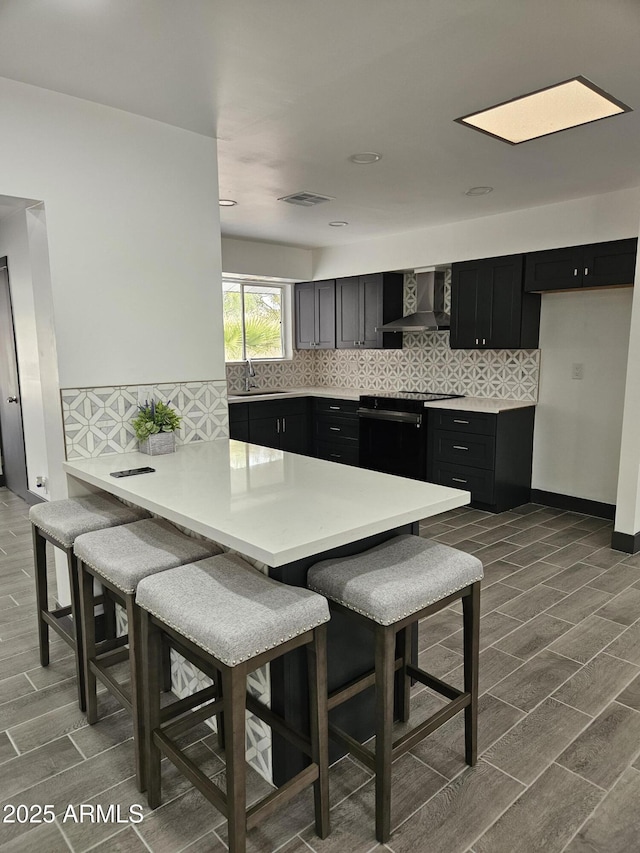 kitchen with black electric range, a sink, dark cabinetry, a peninsula, and wall chimney exhaust hood