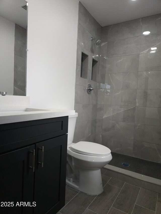 bathroom featuring visible vents, toilet, vanity, and a tile shower