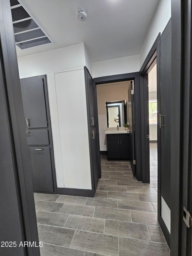 hallway featuring a sink, baseboards, visible vents, and wood tiled floor