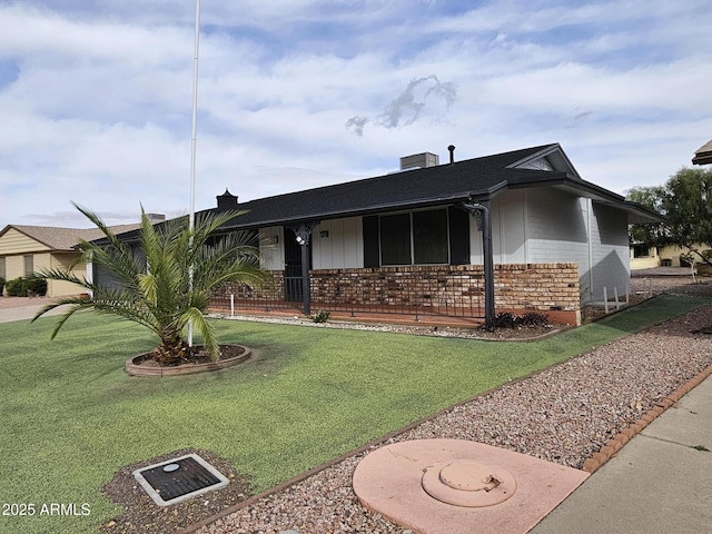 ranch-style home with brick siding, covered porch, a chimney, and a front lawn