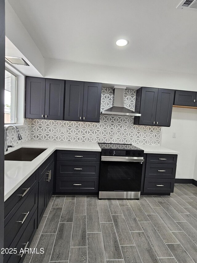 kitchen featuring wall chimney range hood, light countertops, electric range oven, and a sink