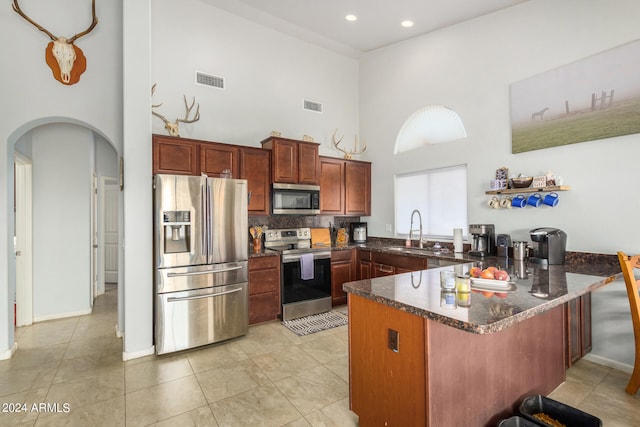 kitchen featuring tasteful backsplash, a high ceiling, sink, appliances with stainless steel finishes, and kitchen peninsula