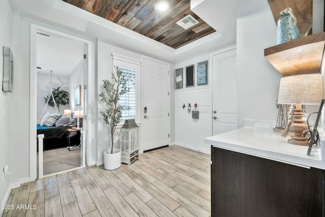 foyer entrance with wood ceiling, light hardwood / wood-style floors, and a raised ceiling