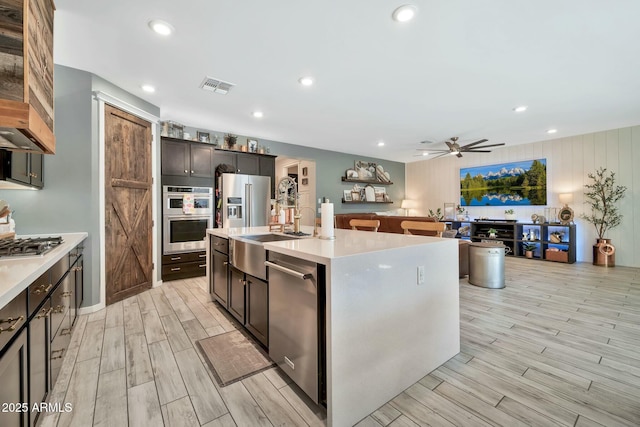 kitchen with ceiling fan, a center island with sink, sink, dark brown cabinetry, and appliances with stainless steel finishes