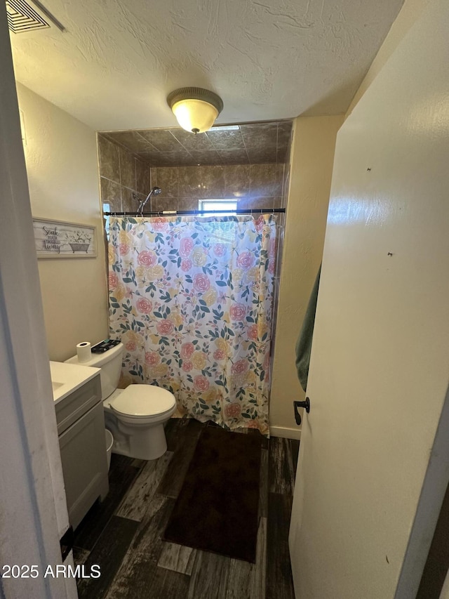 full bathroom featuring a tile shower, a textured ceiling, wood finished floors, and toilet