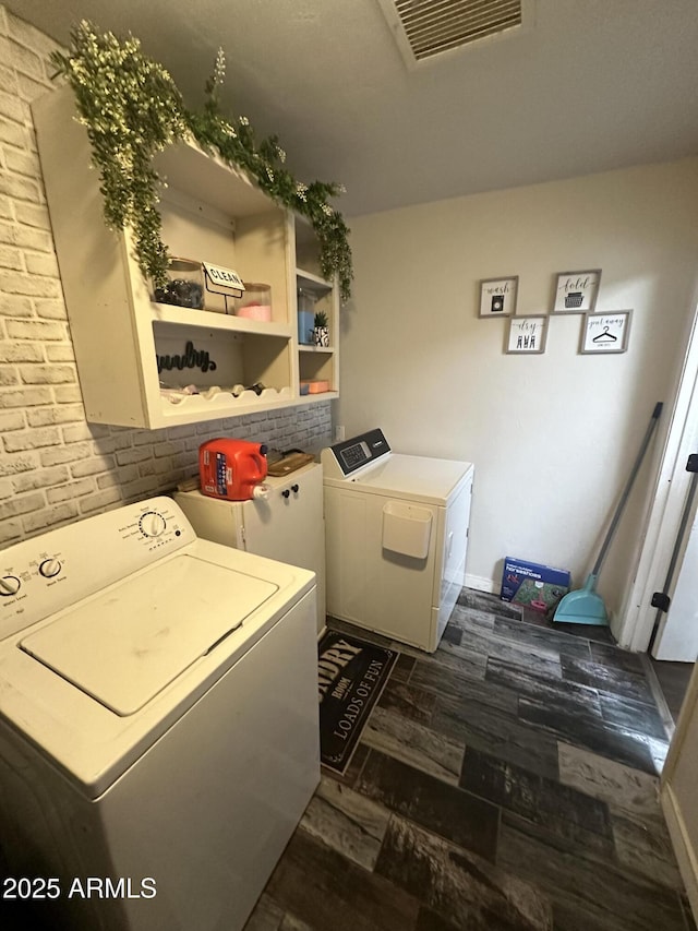 laundry area with washing machine and dryer, brick wall, laundry area, dark wood-style flooring, and visible vents