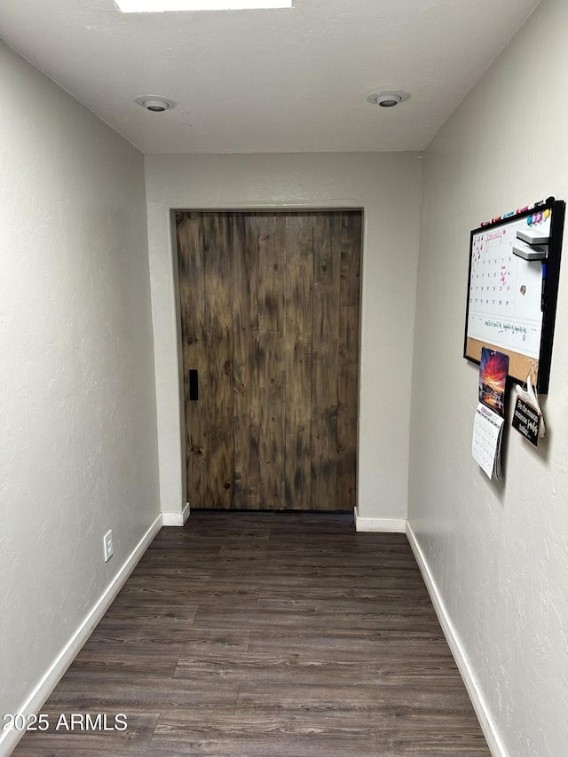 unfurnished room featuring a textured wall, wood finished floors, and baseboards