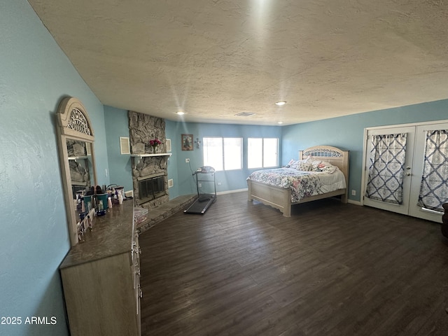 bedroom with a textured ceiling, a stone fireplace, wood finished floors, baseboards, and french doors