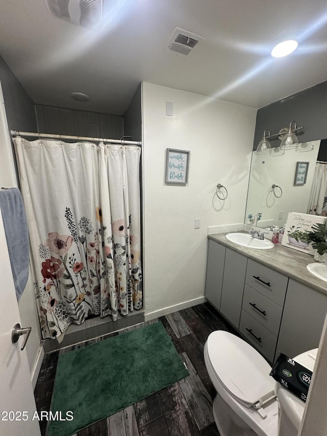 full bath with toilet, wood finished floors, a sink, visible vents, and double vanity