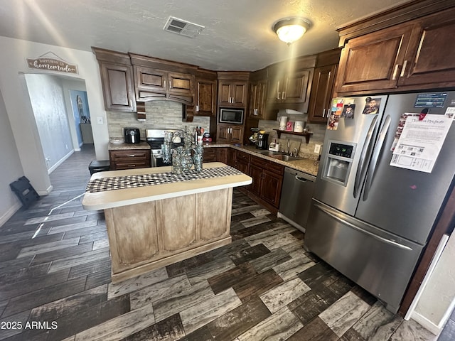 kitchen with visible vents, appliances with stainless steel finishes, a sink, light countertops, and backsplash