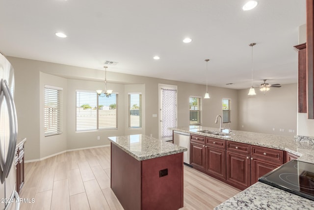 kitchen with stainless steel appliances, light stone counters, decorative light fixtures, a kitchen island with sink, and ceiling fan with notable chandelier