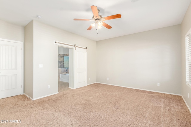 unfurnished bedroom featuring ceiling fan, a barn door, light colored carpet, and ensuite bathroom