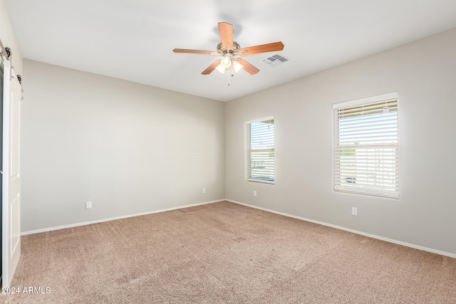 spare room with a barn door, ceiling fan, and carpet floors