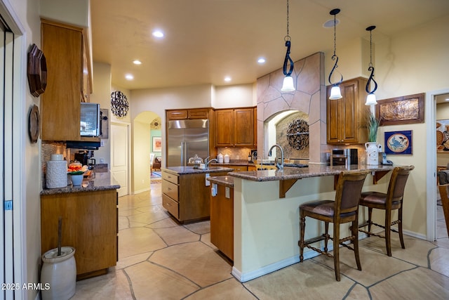 kitchen featuring built in refrigerator, dark stone countertops, tasteful backsplash, kitchen peninsula, and pendant lighting