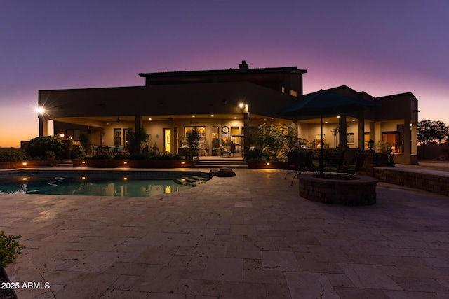 pool at dusk with an outdoor fire pit and a patio area