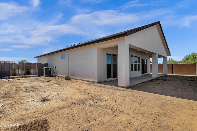 rear view of house with stucco siding, a patio, central AC, and a fenced backyard