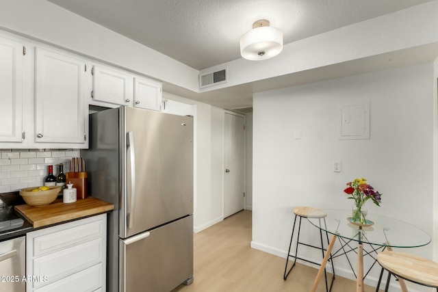 kitchen featuring white cabinetry, stainless steel fridge, decorative backsplash, a textured ceiling, and light hardwood / wood-style flooring