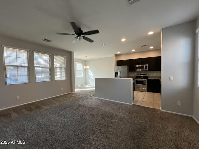 kitchen with open floor plan, stainless steel appliances, dark cabinetry, and light colored carpet