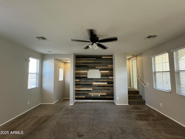 unfurnished living room with an accent wall, stairway, carpet, and visible vents