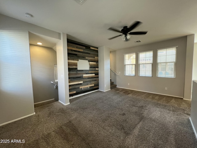 spare room with an accent wall, wood walls, visible vents, stairway, and dark colored carpet