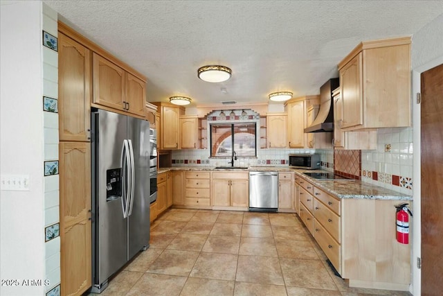 kitchen featuring appliances with stainless steel finishes, light stone counters, wall chimney range hood, light brown cabinets, and a sink