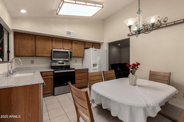 kitchen featuring brown cabinetry, visible vents, a chandelier, appliances with stainless steel finishes, and a sink