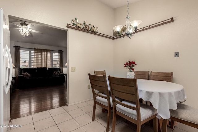 dining room featuring a towering ceiling, ceiling fan with notable chandelier, baseboards, and light tile patterned flooring