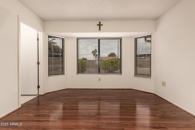 empty room with a wealth of natural light, a textured ceiling, and wood finished floors