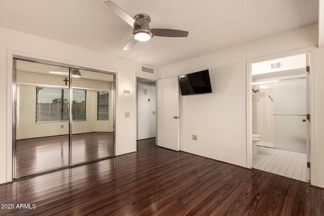 unfurnished bedroom featuring a textured ceiling, a closet, dark wood-style floors, and visible vents