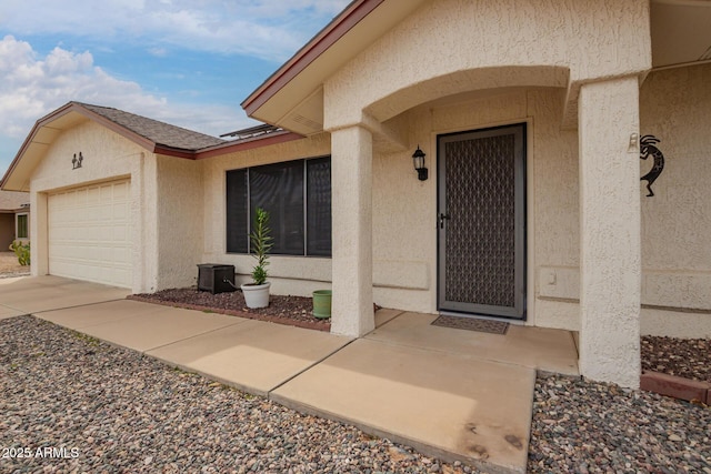 entrance to property with an attached garage, driveway, and stucco siding