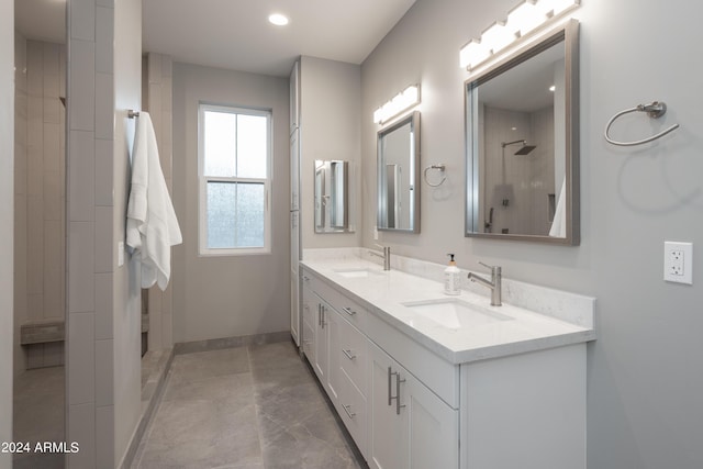 full bathroom with double vanity, tiled shower, baseboards, and a sink