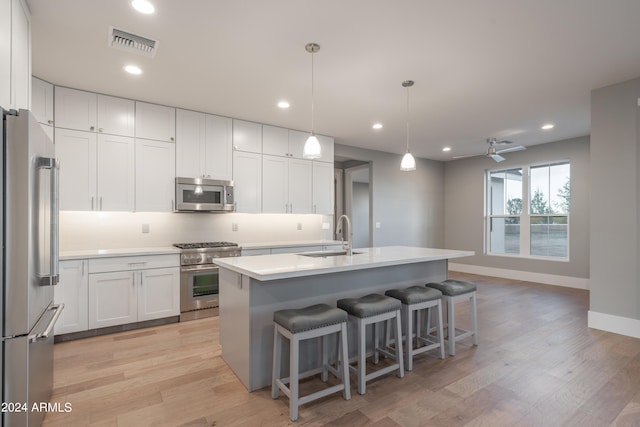 kitchen featuring white cabinets, an island with sink, hanging light fixtures, sink, and premium appliances