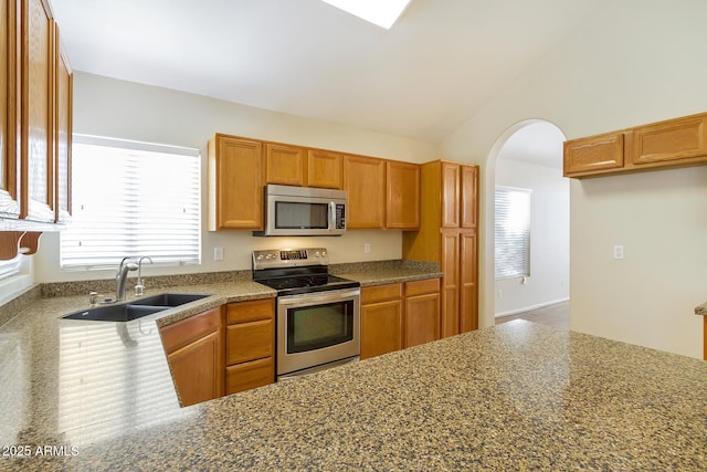 kitchen featuring lofted ceiling, brown cabinets, arched walkways, stainless steel appliances, and a sink