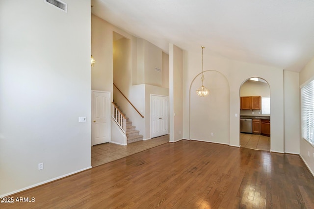 unfurnished living room featuring visible vents, arched walkways, stairs, hardwood / wood-style flooring, and a notable chandelier