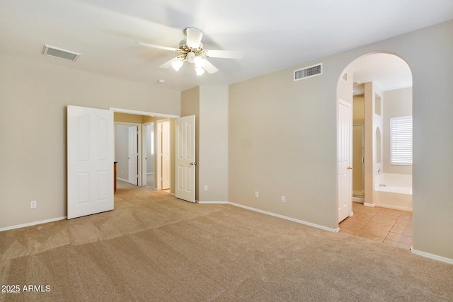 unfurnished bedroom featuring visible vents, carpet, arched walkways, and baseboards