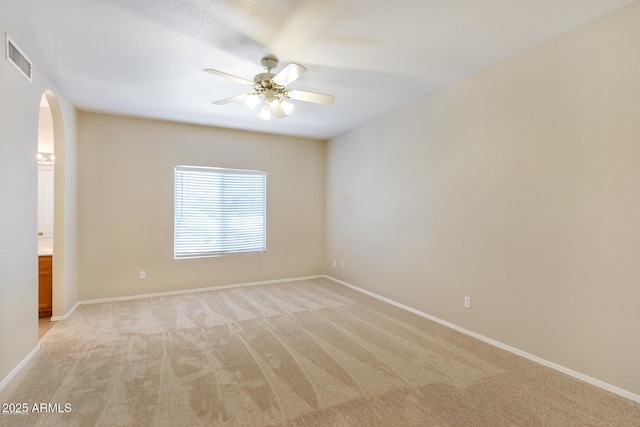 spare room featuring visible vents, arched walkways, baseboards, light colored carpet, and ceiling fan