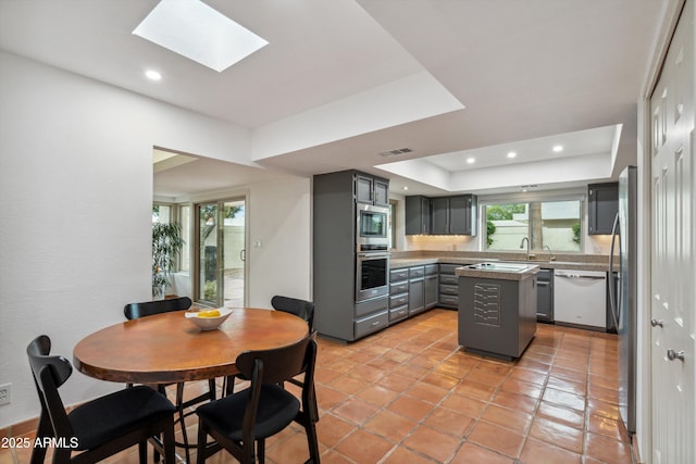 kitchen featuring visible vents, a skylight, appliances with stainless steel finishes, a raised ceiling, and gray cabinetry