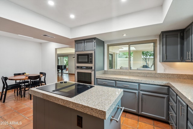 kitchen with wall oven, visible vents, a kitchen island, stainless steel microwave, and black electric stovetop