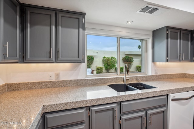 kitchen featuring visible vents, light countertops, a sink, white dishwasher, and gray cabinetry
